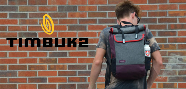 Merch Outfitters - Example Image of Branded Corporate Goods & Branding Items - Timbuk2 logo and man wearing backpack in front of brick wall